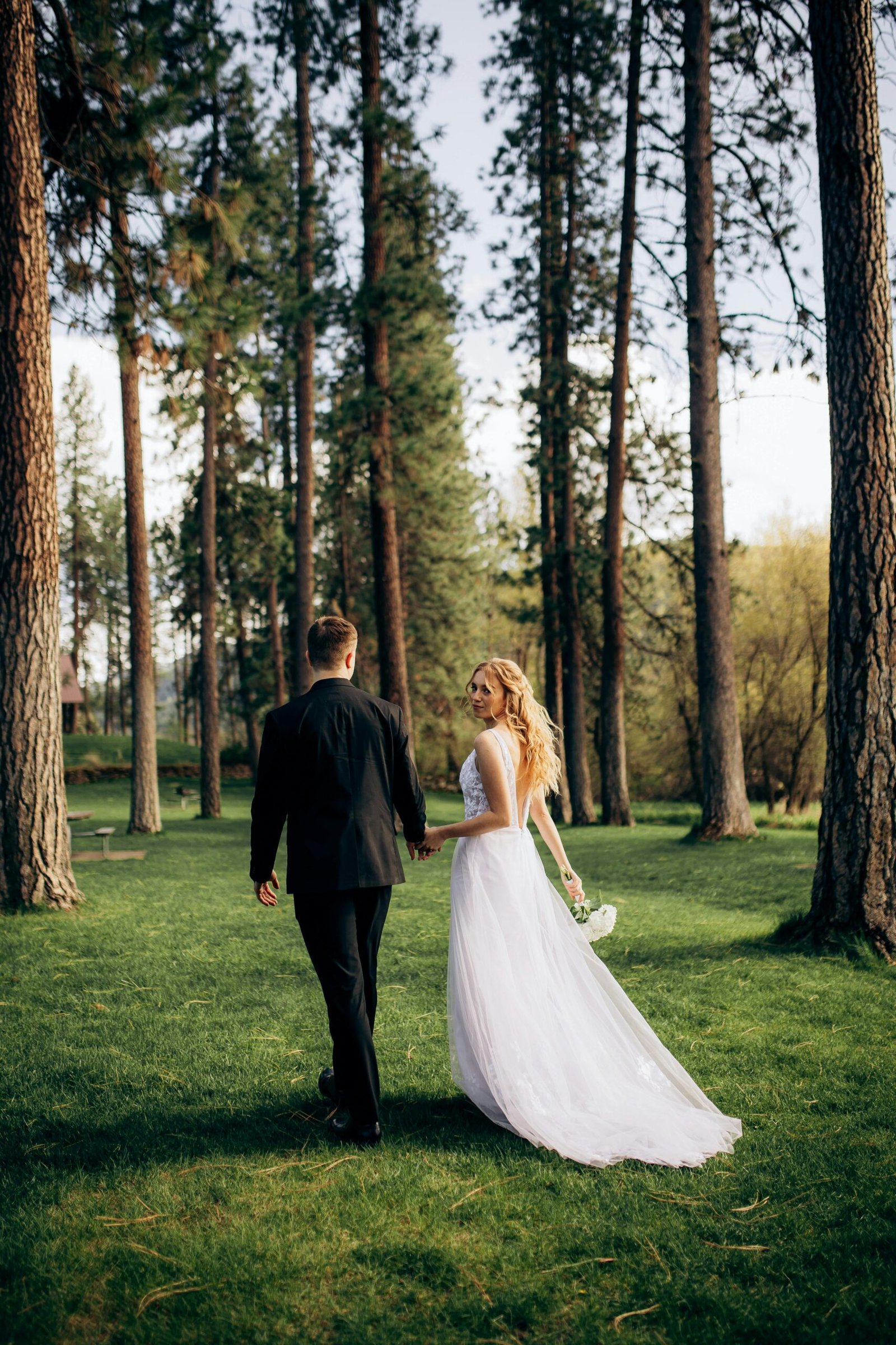 A newlywed couple walks hand in hand through a scenic Idaho forest on their wedding day.