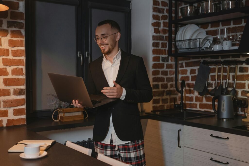 Man in suit jacket and shorts videoconferencing from home kitchen during night.